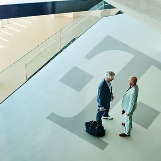 Sicht von oben auf einen weiten Flur mit großem Telekom Logo: Zwei Personen unterhalten sich