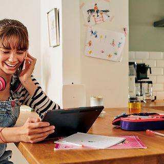 Junge Frau telefoniert mit Smartphone während sie aufs Tablet schaut. 
