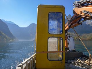 Yellow telephone box being transported by boat across the Königssee in Bavaria.